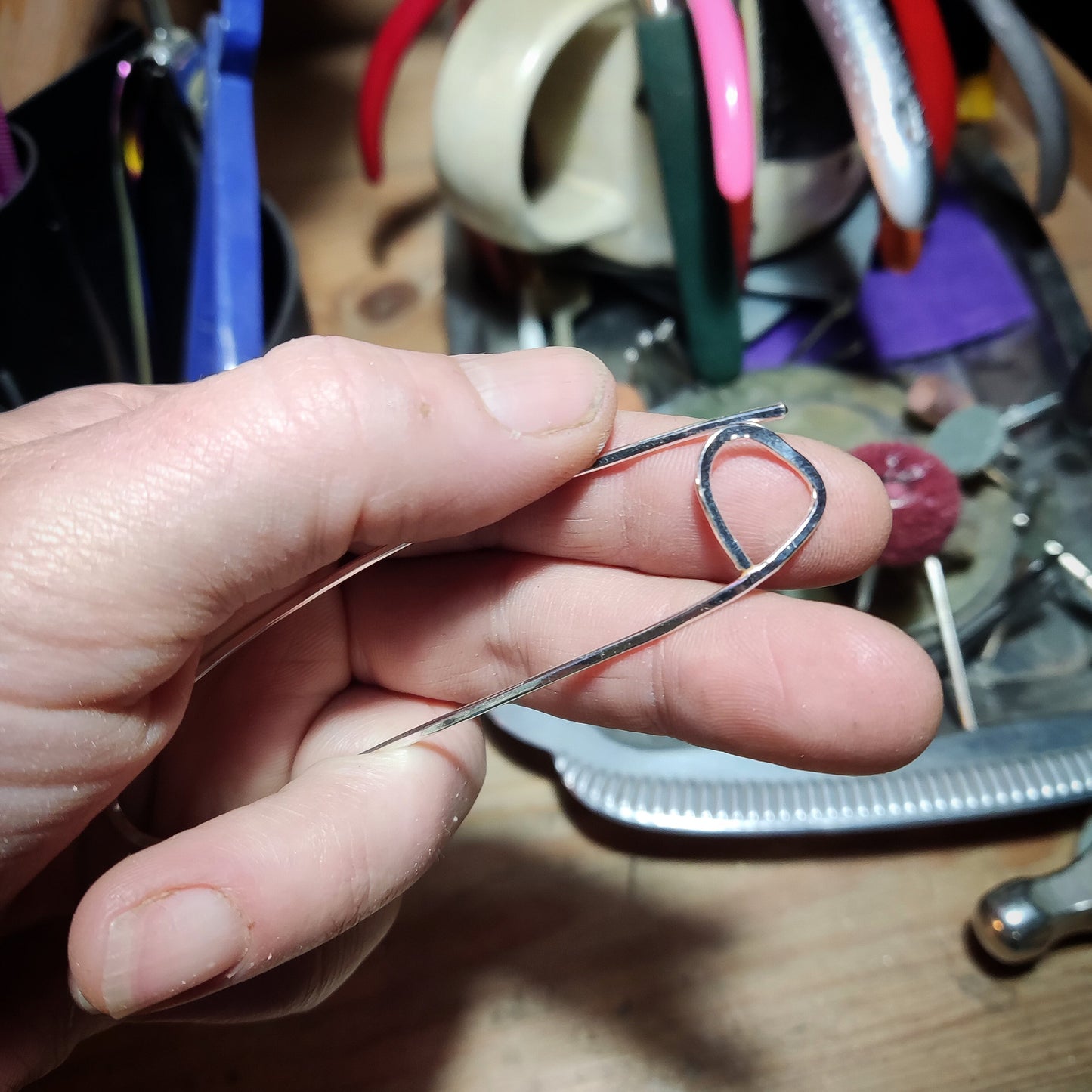 hand holding a knitting stitch marker with tools in the background
