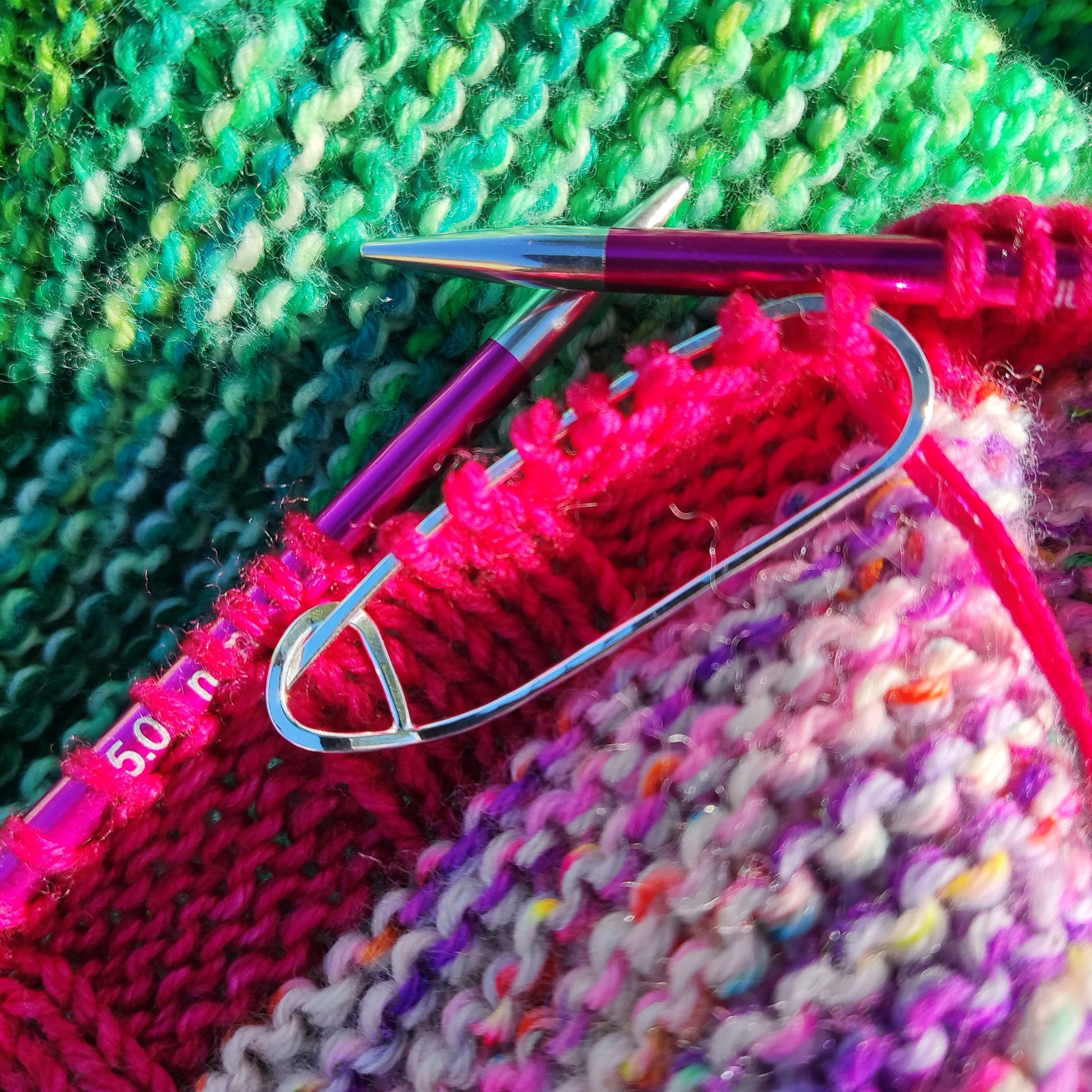 A silver stitch holder on a colourful knitting project.