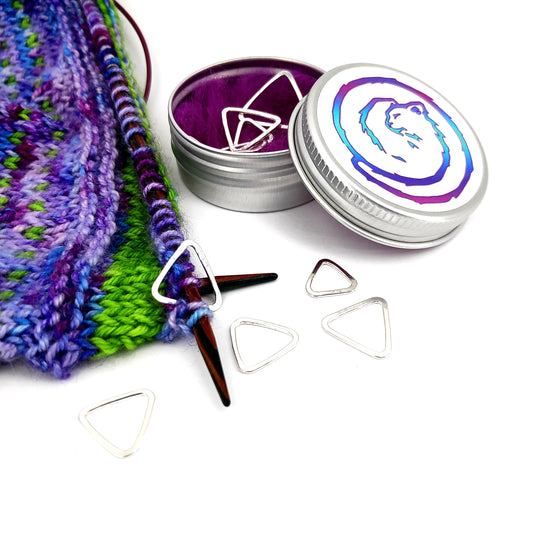 Sterling Silver triangular stitch markers of various sizes, pictured with a Fizzy Stitches branded tin and colourful knitting.